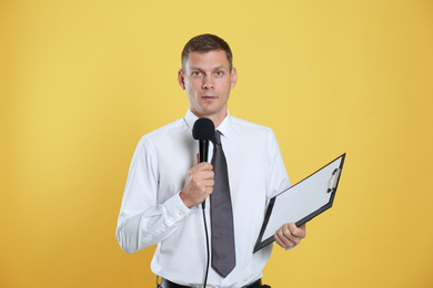 Photo of Male journalist with microphone and clipboard on yellow background