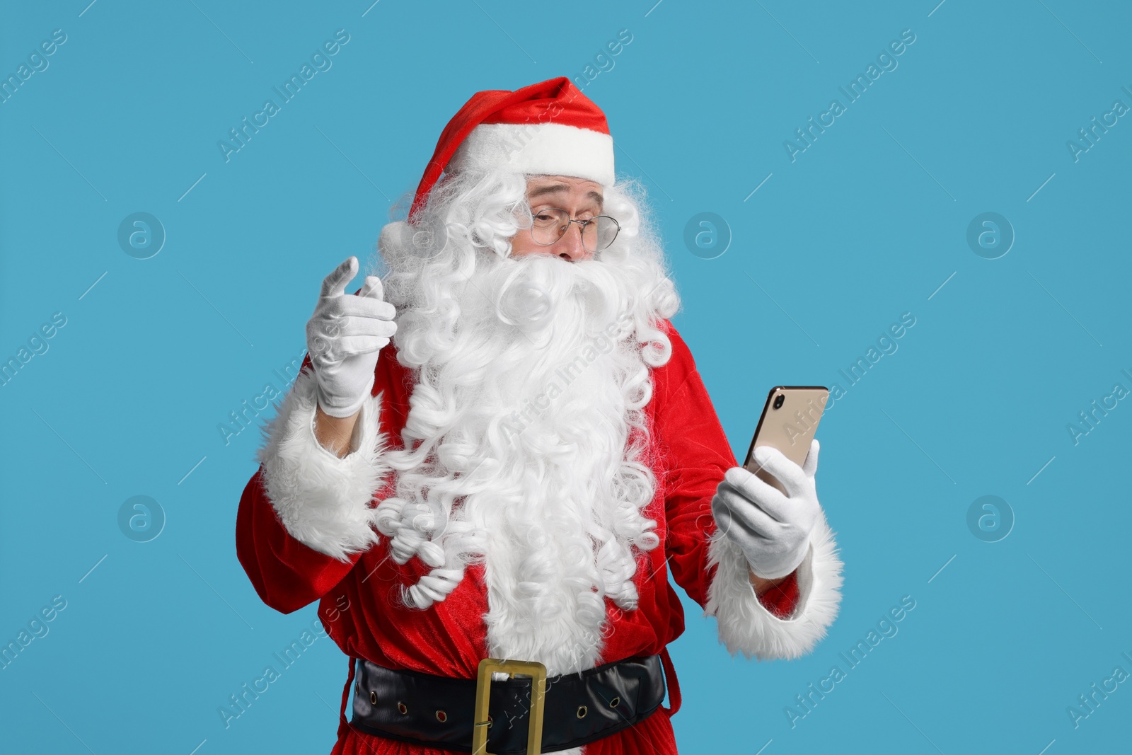 Photo of Merry Christmas. Santa Claus using smartphone on light blue background