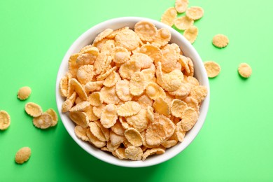 Photo of Bowl of tasty crispy corn flakes on light green background, flat lay