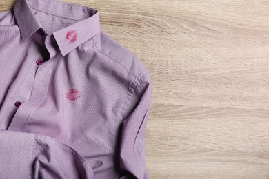 Photo of Men's shirt with lipstick kiss marks on wooden background, top view. Space for text