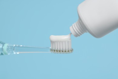 Photo of Squeezing toothpaste onto electric toothbrush on light blue background, closeup