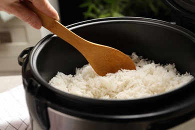 Photo of Woman taking tasty rice with spoon from cooker in kitchen, closeup