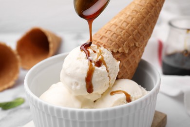 Photo of Pouring caramel sauce onto ice cream on table, closeup