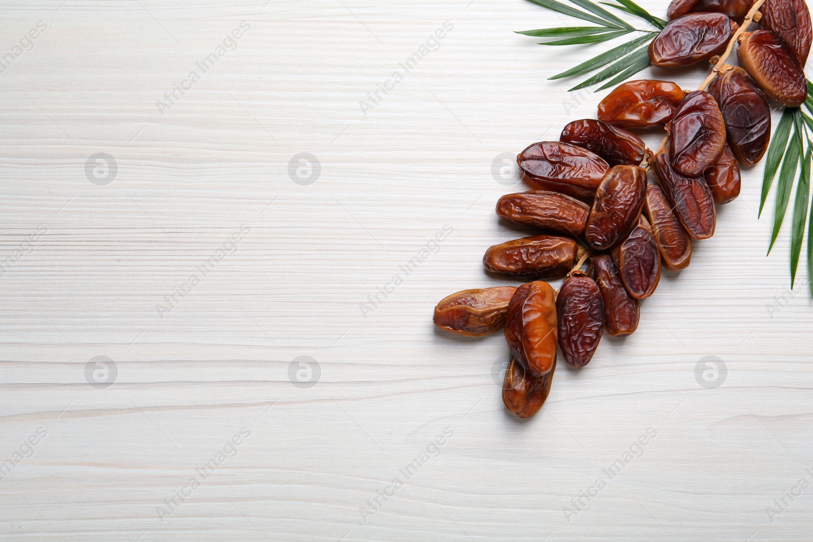 Photo of Branch of sweet dried dates with green leaves on white wooden table, flat lay. Space for text