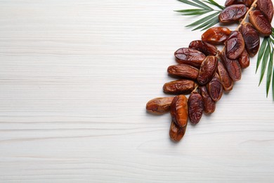 Photo of Branch of sweet dried dates with green leaves on white wooden table, flat lay. Space for text