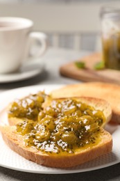 Photo of Slice of toasted bread with gooseberry jam on grey table, closeup