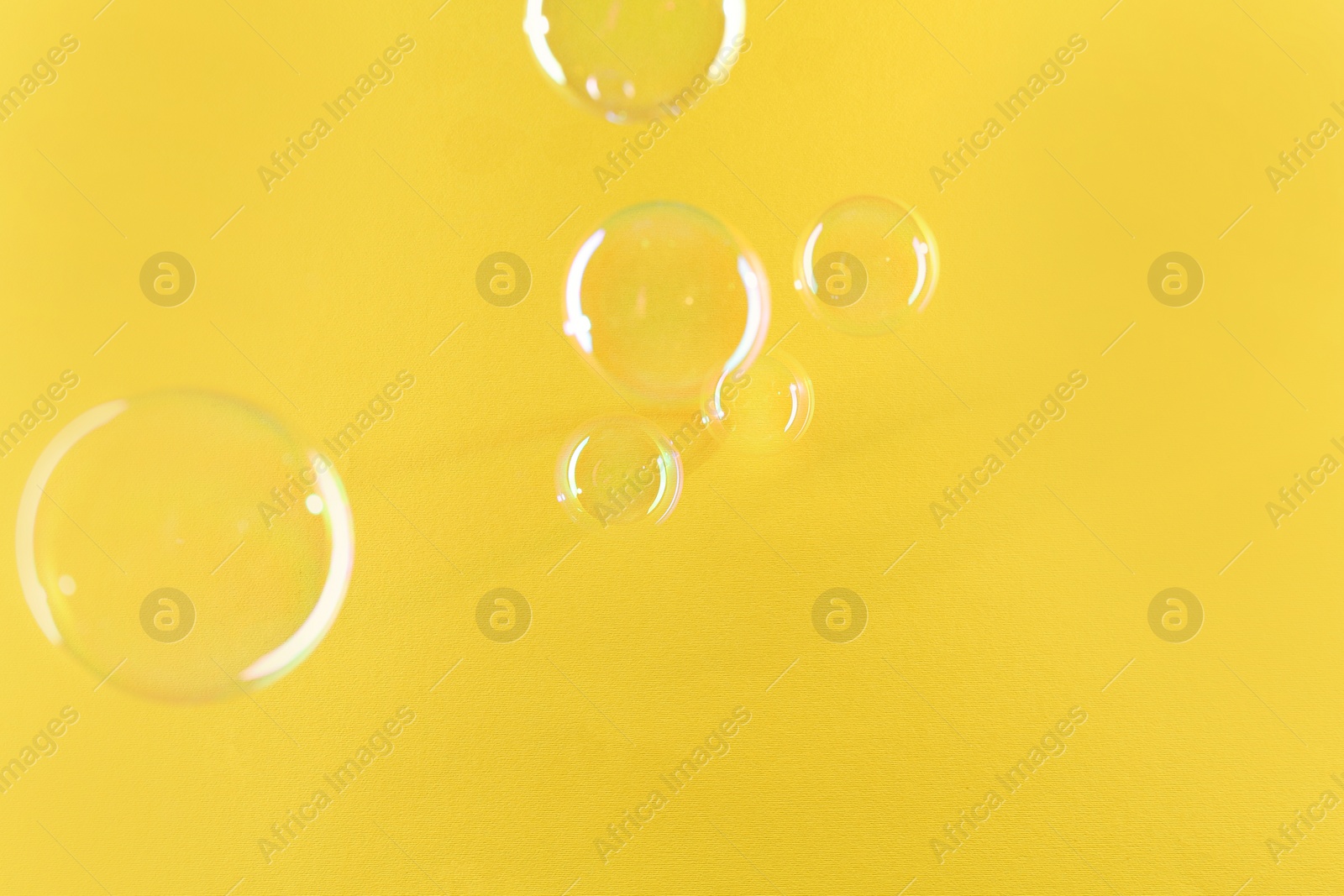 Photo of Beautiful transparent soap bubbles on yellow background