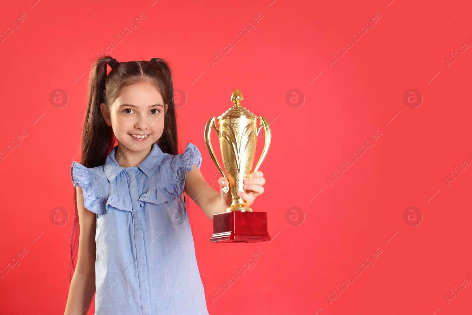 Photo of Happy girl with golden winning cup on red background. Space for text