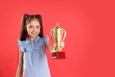 Photo of Happy girl with golden winning cup on red background. Space for text