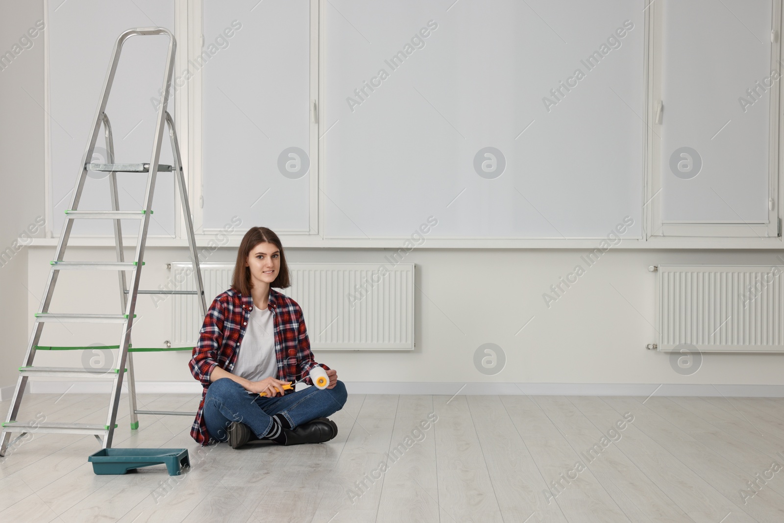 Photo of Young woman with roller sitting near stepladder indoors. Room renovation