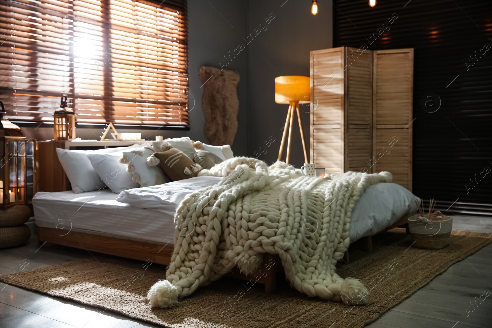 Photo of Cozy bedroom interior with knitted blanket and cushions