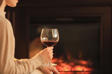 Young woman with glass of wine near fireplace indoors, closeup. Cozy atmosphere