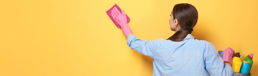Image of Woman with basin of detergents cleaning yellow wall, space for text. Banner design