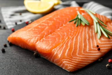 Photo of Fresh salmon fillet with rosemary on slate board, closeup