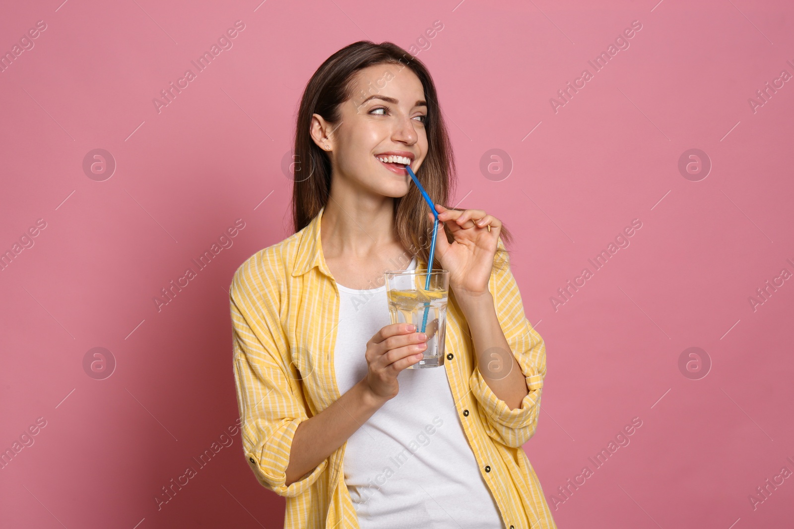 Photo of Young woman drinking lemon water on pink background