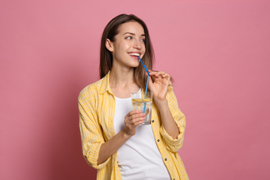 Young woman drinking lemon water on pink background