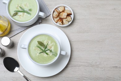 Delicious asparagus soup with green onion served on white wooden table, flat lay. Space for text