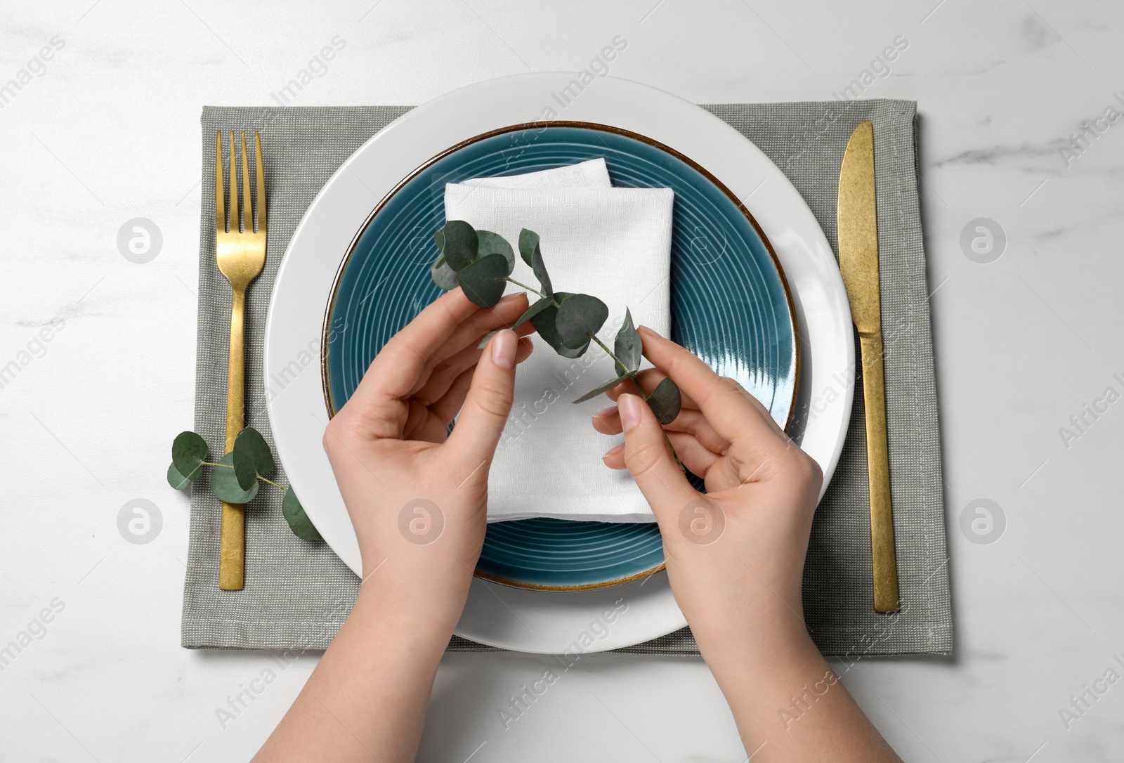 Photo of Woman adjusting stylish setting with eucalyptus leaves on white marble table, closeup