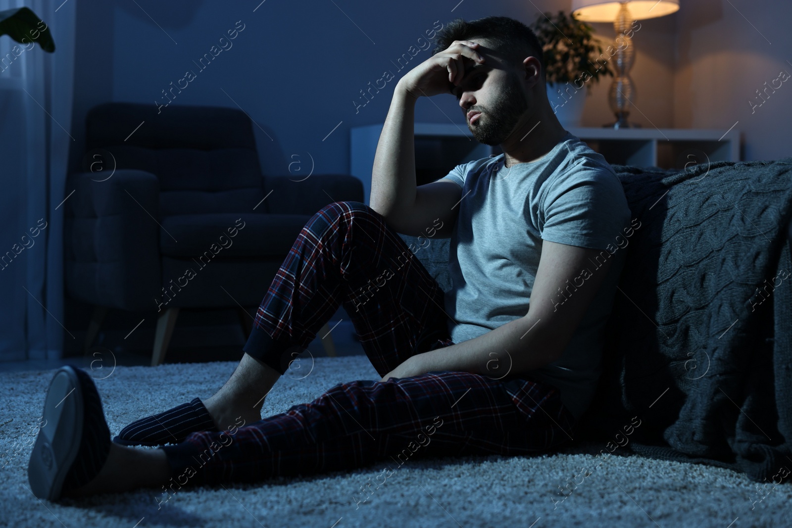 Photo of Tired man sitting on carpet at night