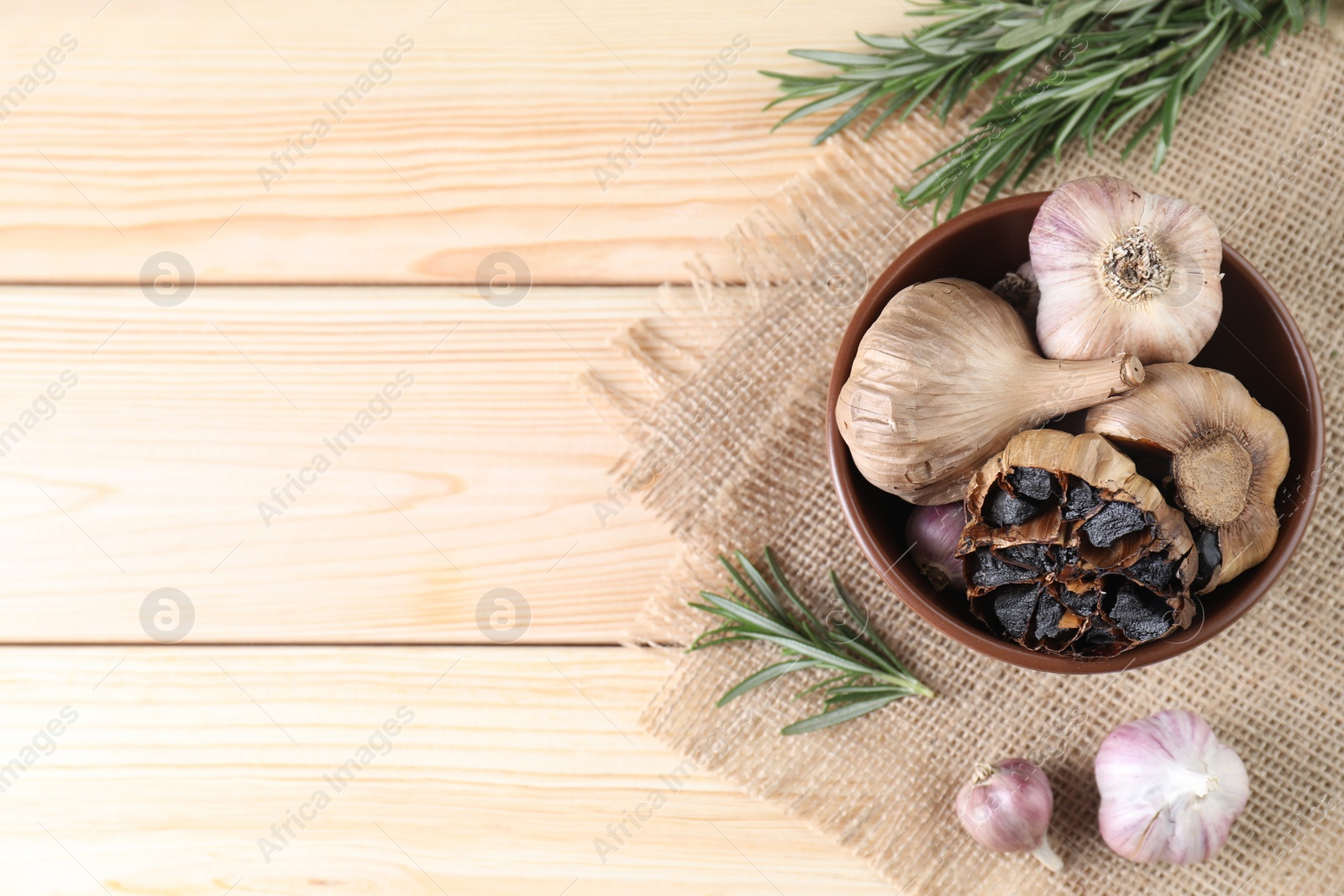 Photo of Bulbs of fresh and fermented black garlic on wooden table, flat lay. Space for text