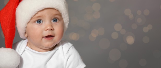 Image of Cute baby wearing Santa hat against blurred lights, banner design with space for text. Christmas celebration