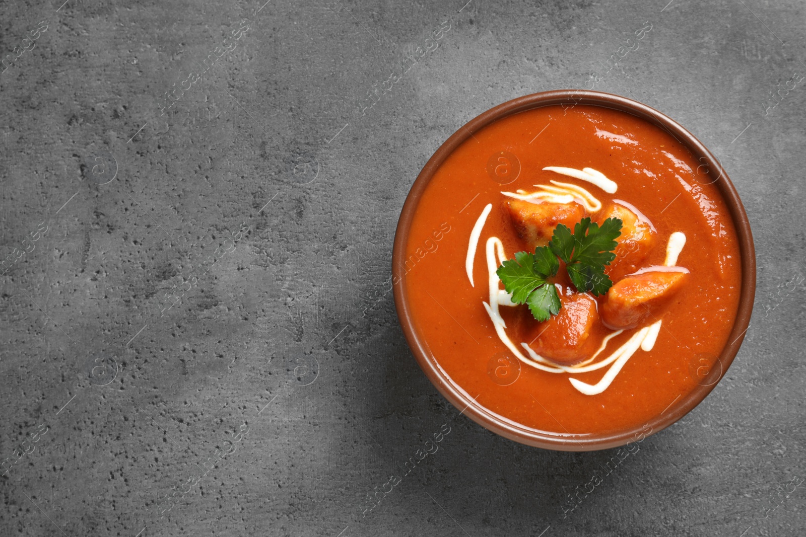 Photo of Bowl of delicious butter chicken on grey background, top view with space for text. Traditional indian Murgh Makhani