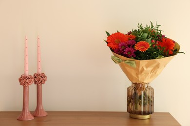 Photo of Bouquet of flowers and candles on wooden table near white wall