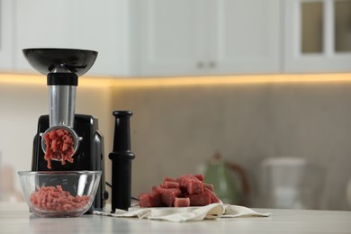 Electric meat grinder with beef mince on white table in kitchen, space for text