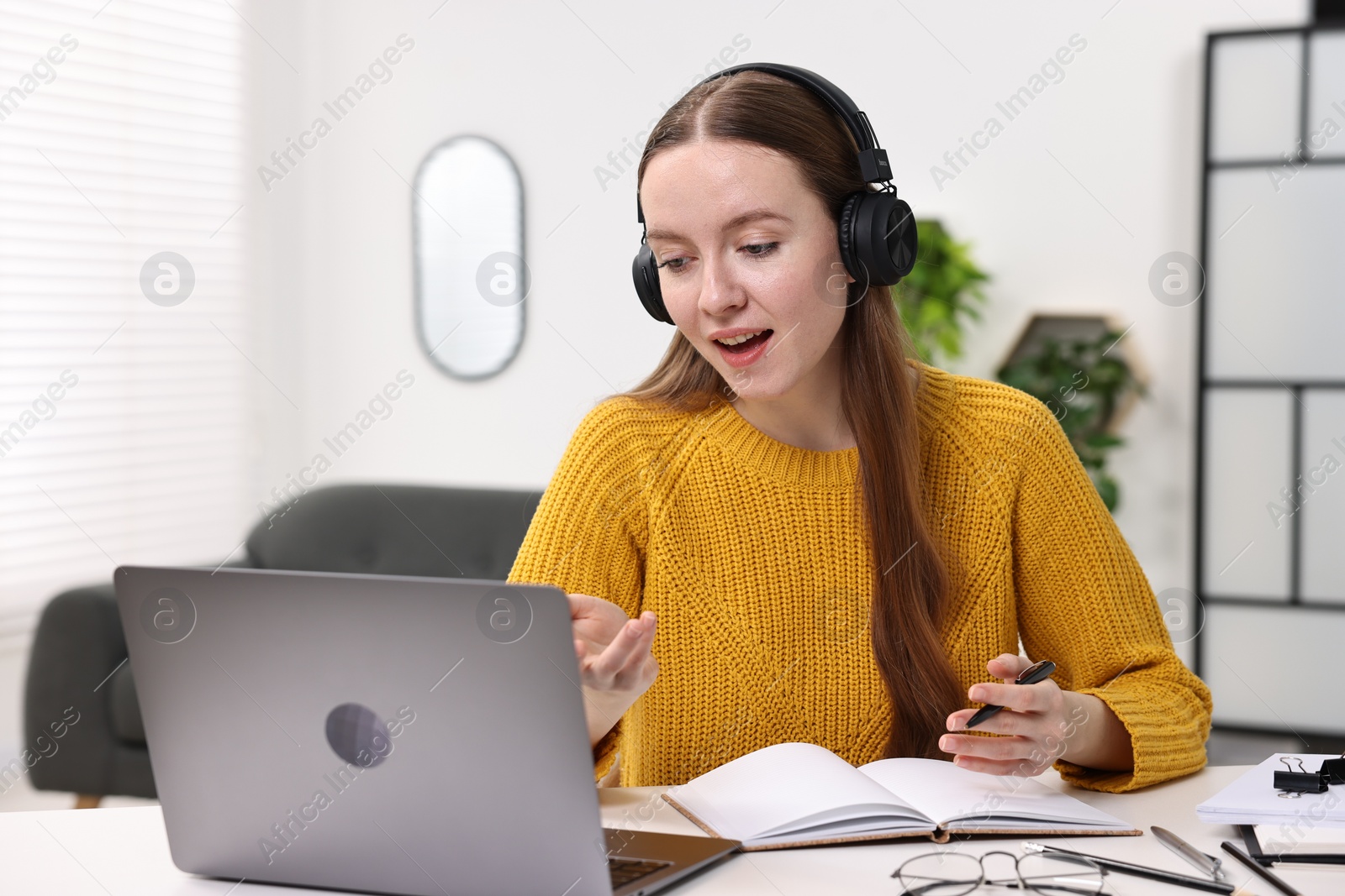 Photo of E-learning. Young woman using laptop during online lesson at white table indoors