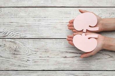 Photo of Woman holding paper cutout of kidneys at white wooden table, top view. Space for text