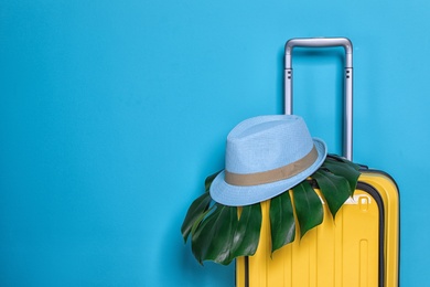 Photo of Bright yellow suitcase with hat and tropical leaf on color background