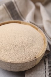 Photo of Granulated yeast in wooden bowl on table, closeup