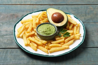 Photo of Plate with french fries, guacamole dip, parsley and avocado served on grey wooden table