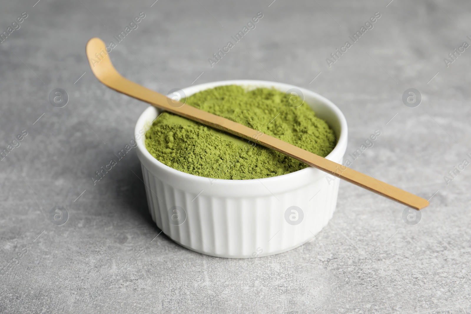 Photo of Green matcha powder and bamboo scoop on light grey table, closeup