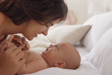 Happy young mother with her cute baby on bed indoors