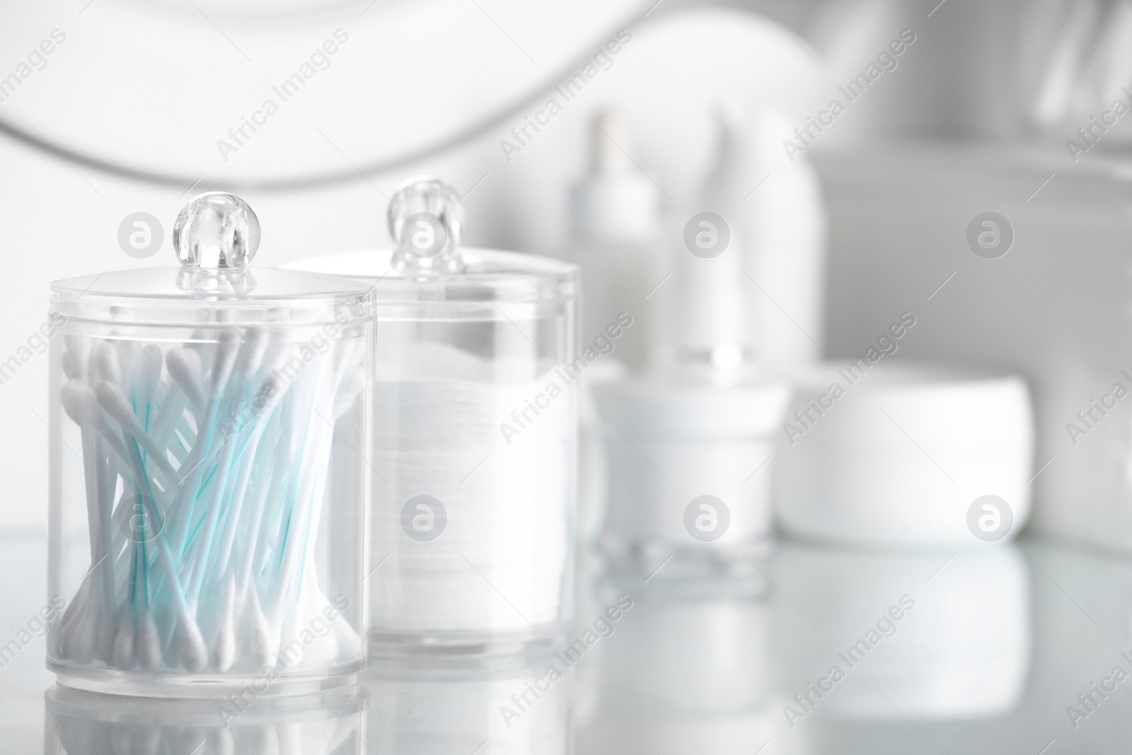 Photo of Containers with cotton swabs and pads near cosmetic products on dressing table. Space for text