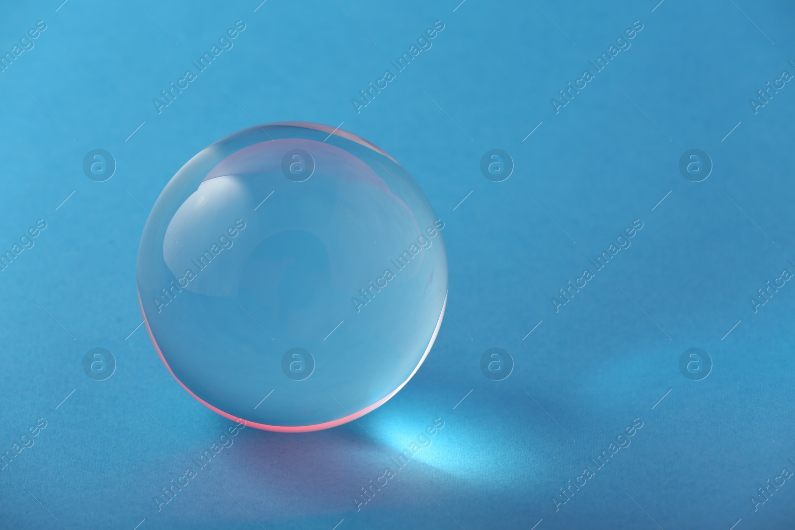 Photo of Transparent glass ball on light blue background. Space for text