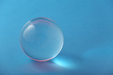 Photo of Transparent glass ball on light blue background. Space for text