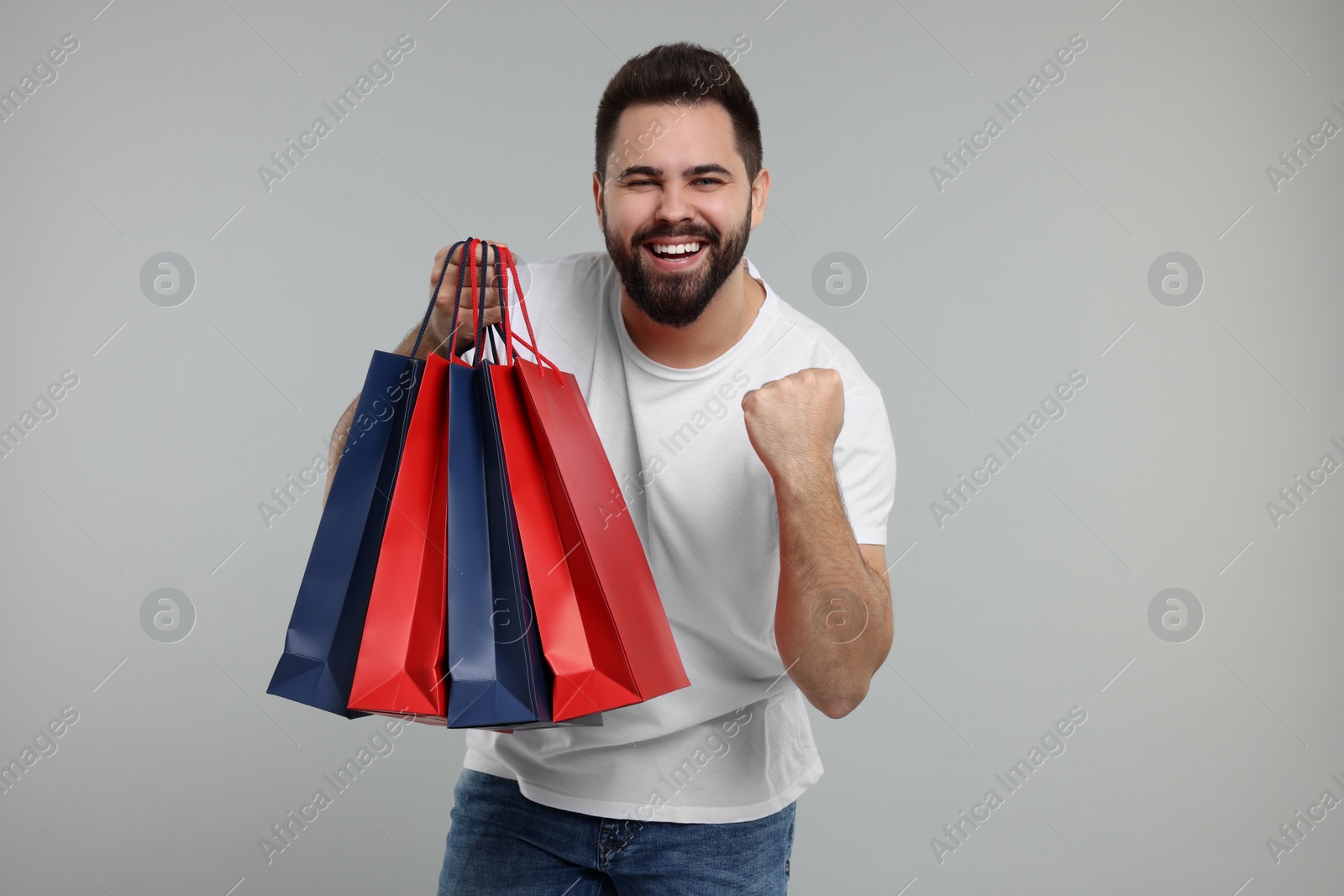 Photo of Happy man with many paper shopping bags on grey background