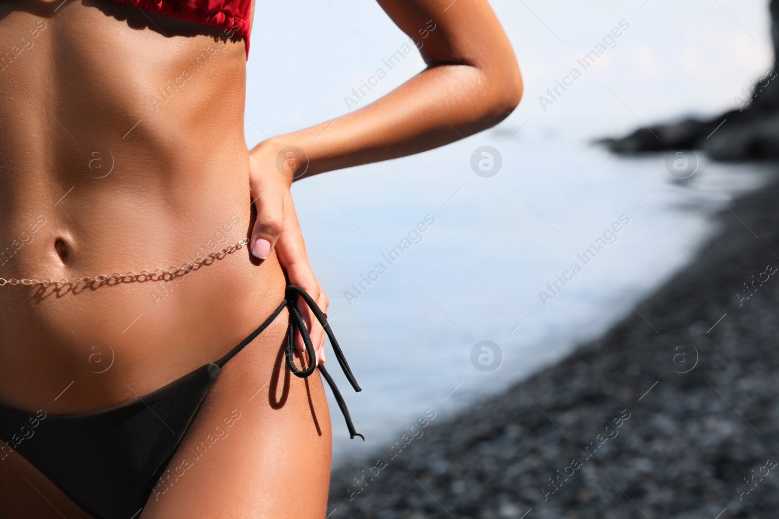 Photo of Sexy young woman in stylish bikini on seashore, closeup. Space for text