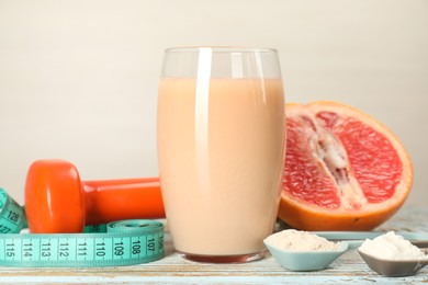 Photo of Tasty shake, grapefruit, dumbbell, scoops with different powders and measuring tape on wooden table, closeup. Weight loss