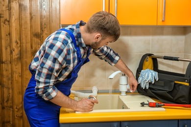 Professional plumber in uniform fixing kitchen sink