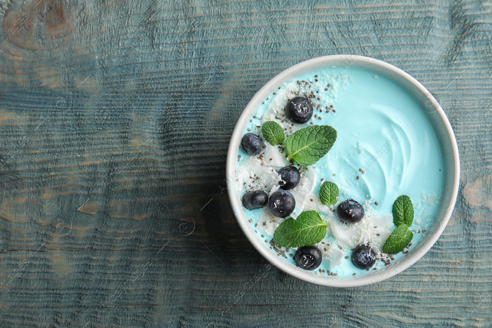 Photo of Bowl of spirulina smoothie on wooden background, top view. Space for text