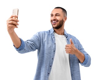 Photo of Smiling young man taking selfie with smartphone and showing thumbs up on white background