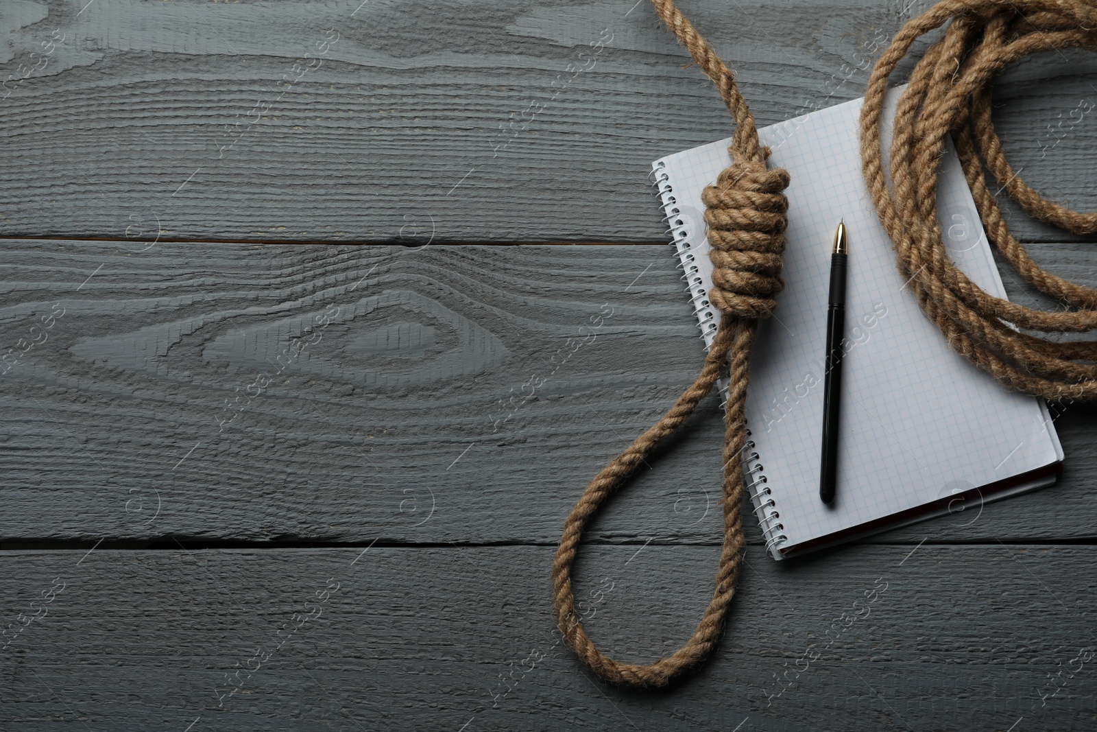 Photo of Rope noose and blank notebook with pen on grey wooden table, flat lay. Space for text