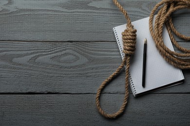 Photo of Rope noose and blank notebook with pen on grey wooden table, flat lay. Space for text