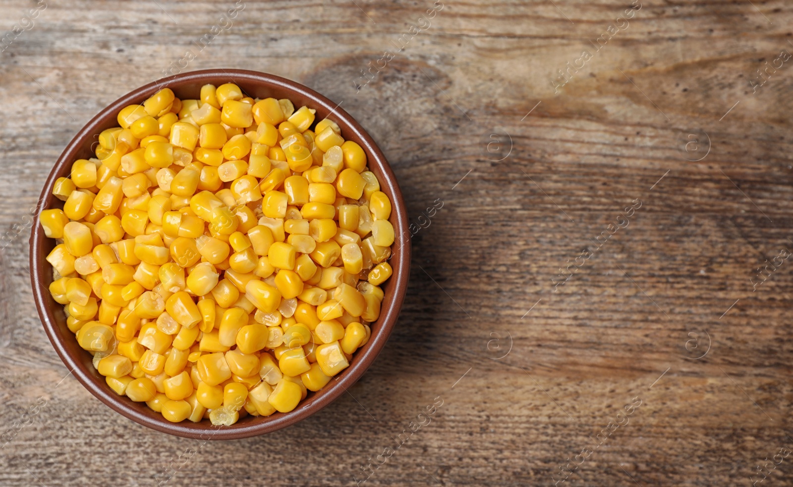 Photo of Delicious canned corn in bowl on wooden table, top view. Space for text