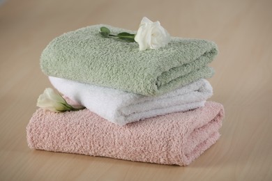 Photo of Soft folded towels with eustoma flowers on wooden table
