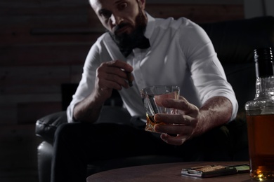 Man with glass of whiskey and cigar sitting at table indoors