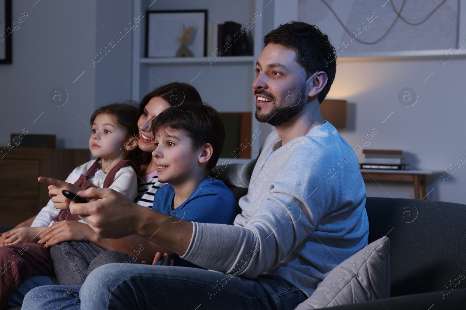 Photo of Happy family watching TV at home in evening. Father changing channels with remote control